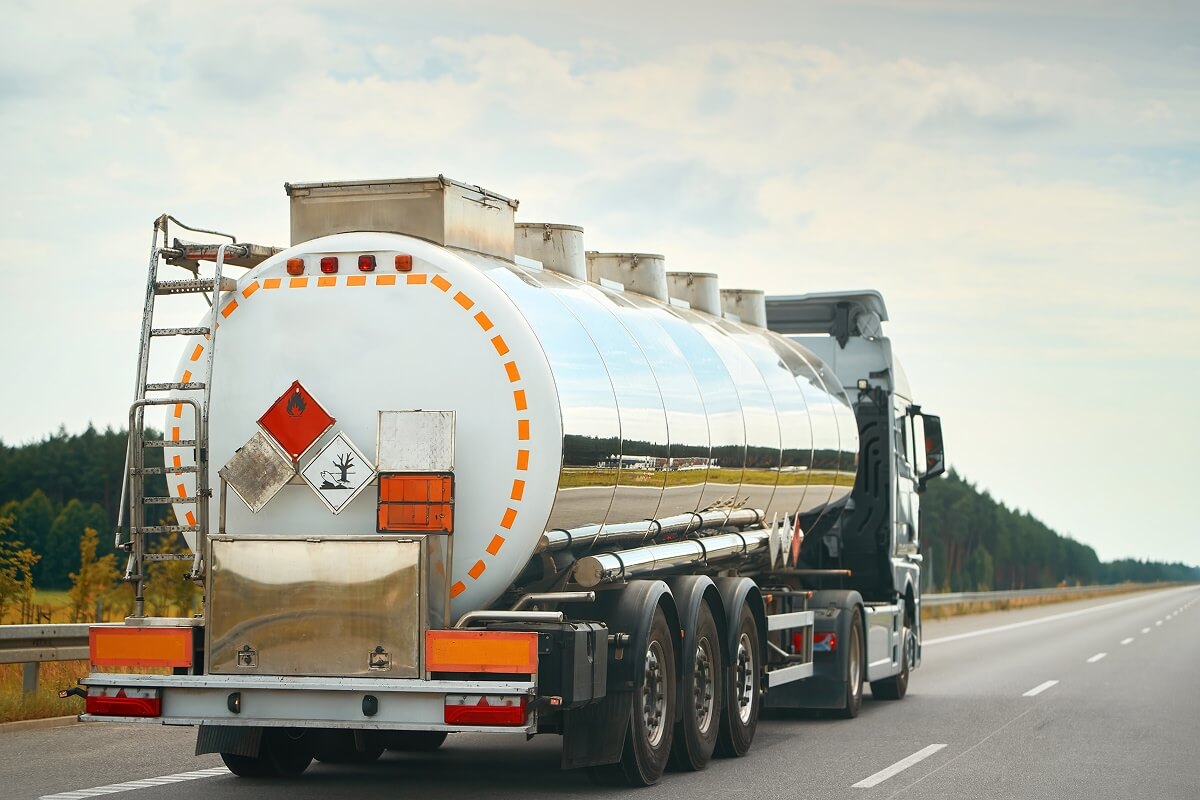 Hazmat-certified LNG tanker truck transporting liquefied natural gas on highway with orange safety markings and warning placards