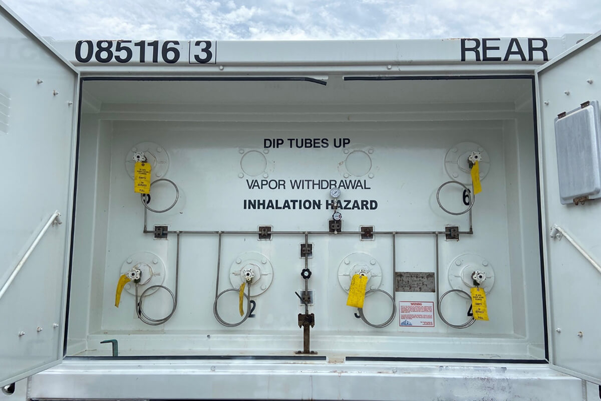 Two white ISO tank containers secured on a flatbed trailer at an industrial site.